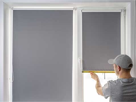 Man installing gray shades on a window and door